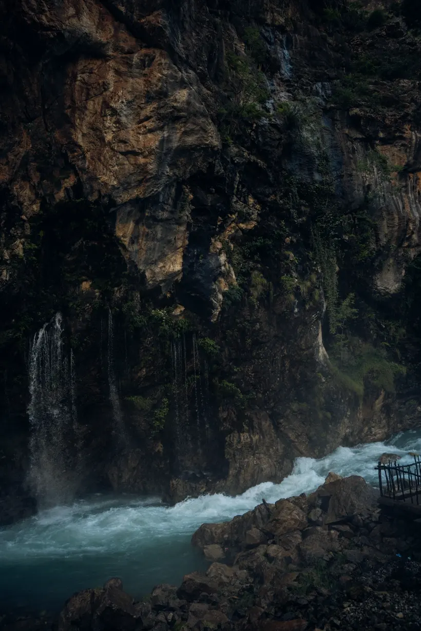 Waterfalls threading down a shaded cliff into a rushing river