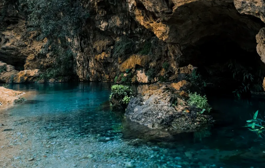 A turquoise spring pool resting under an overhanging limestone cliff
